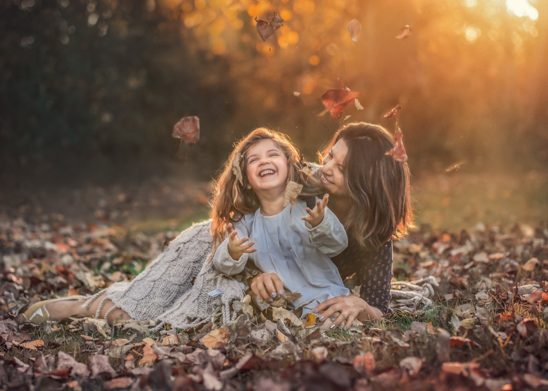 Mamá e hija riendo mientras caen hojas de otoño
