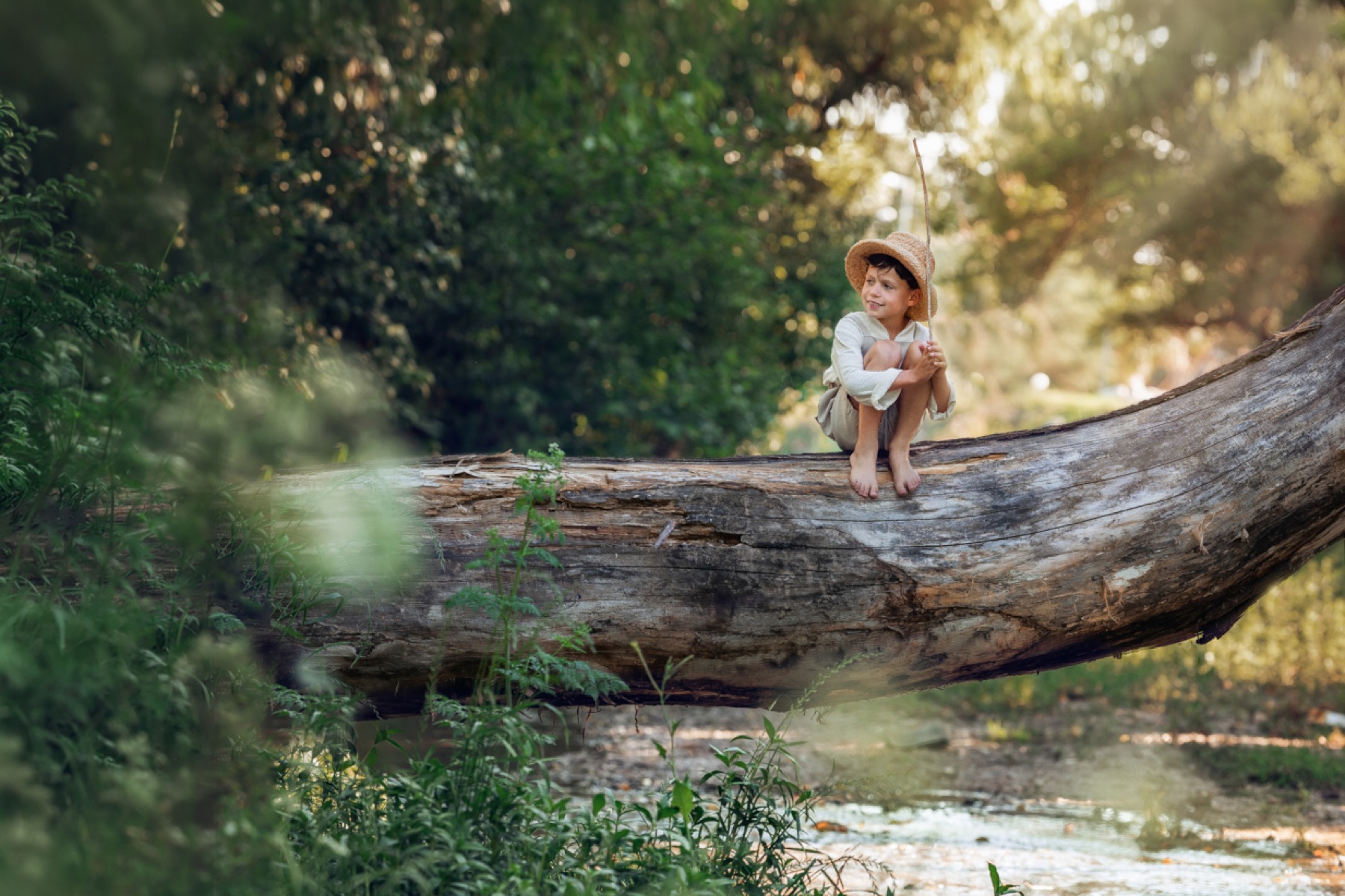 Niño sentado sobre un tronco junto al río