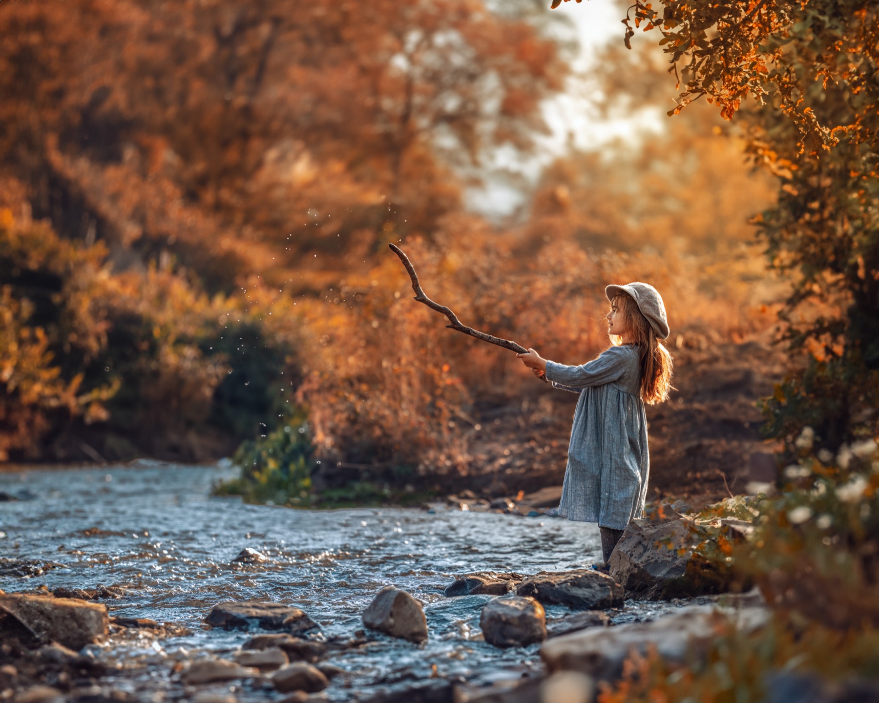 Niña jugando con una vara junto a un río en otoño