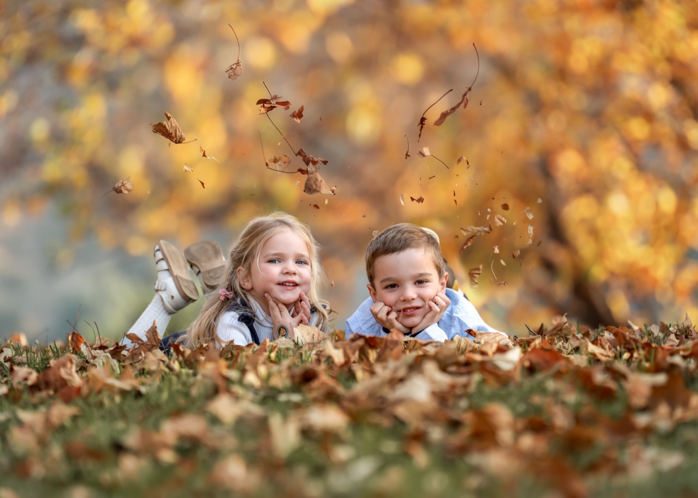 Dos hermanos recostados entre hojas de otoño