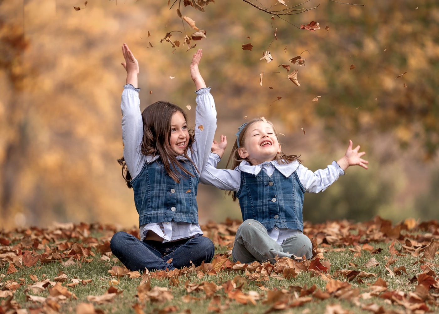 Dos hermanas lanzando hojas de otoño al aire