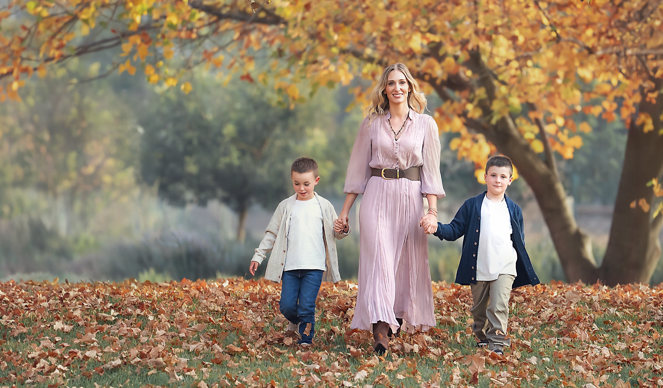 Mamá caminando con sus dos hijos entre hojas de otoño
